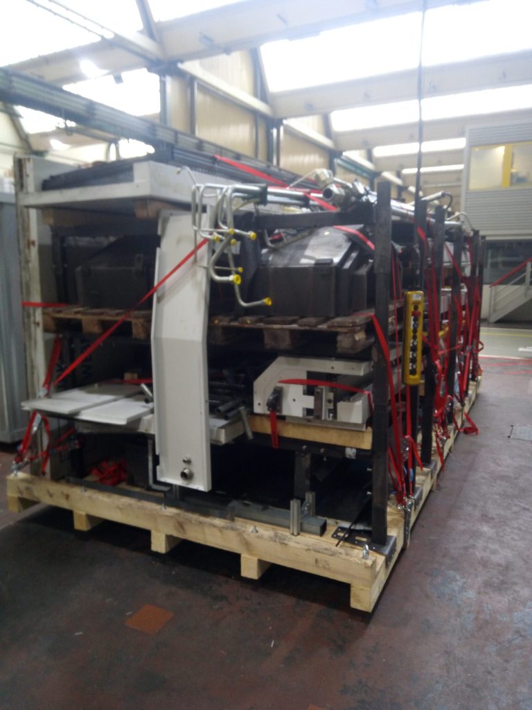 Frontansicht einer Transportpalette mit Palettenaufnahme, hängend gelagerten Hydraulikrohren und verzurrten Maschinenbauteilen